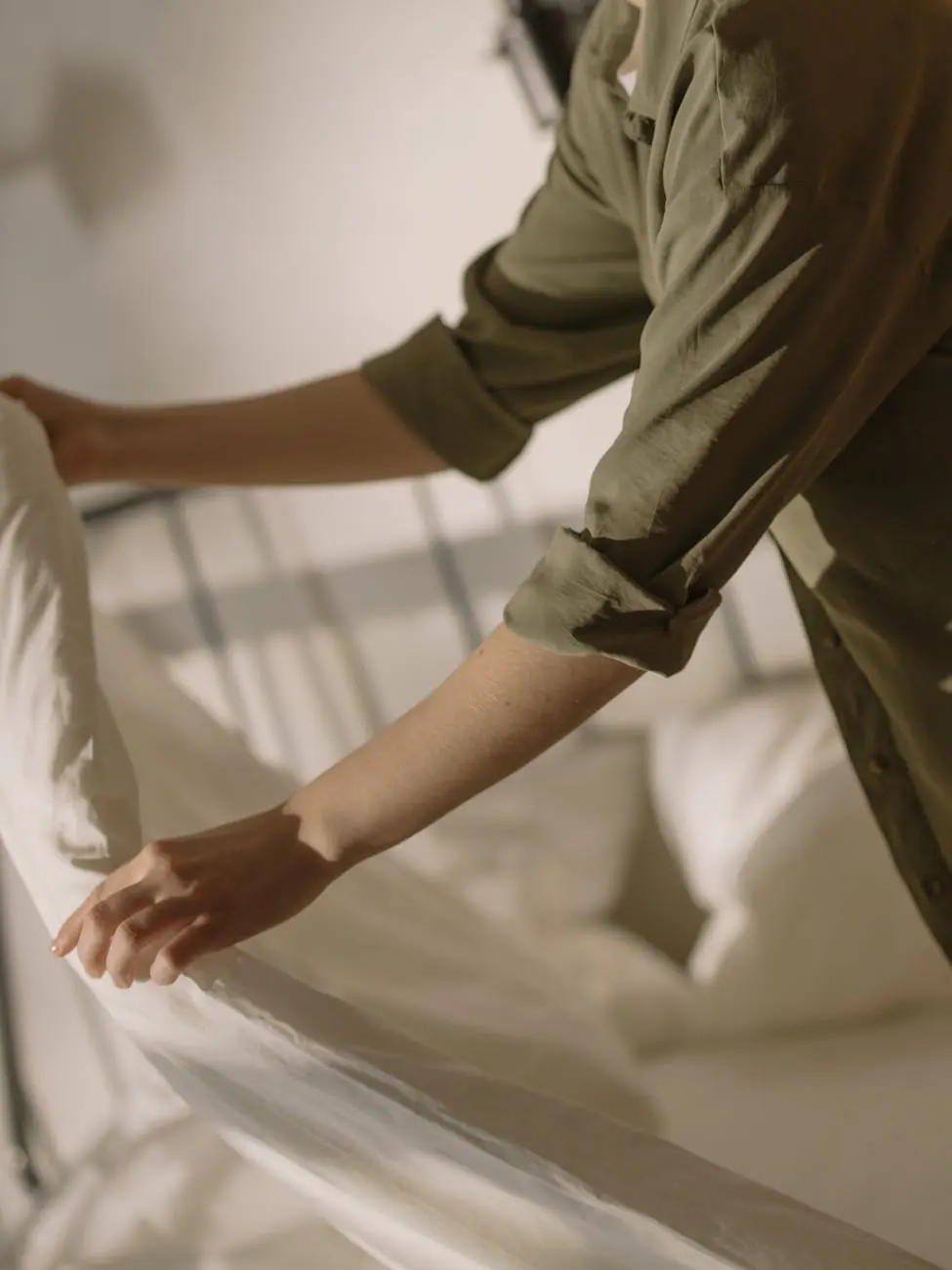 Man in Green Dress Shirt and Brown Pants Sitting on White Bed